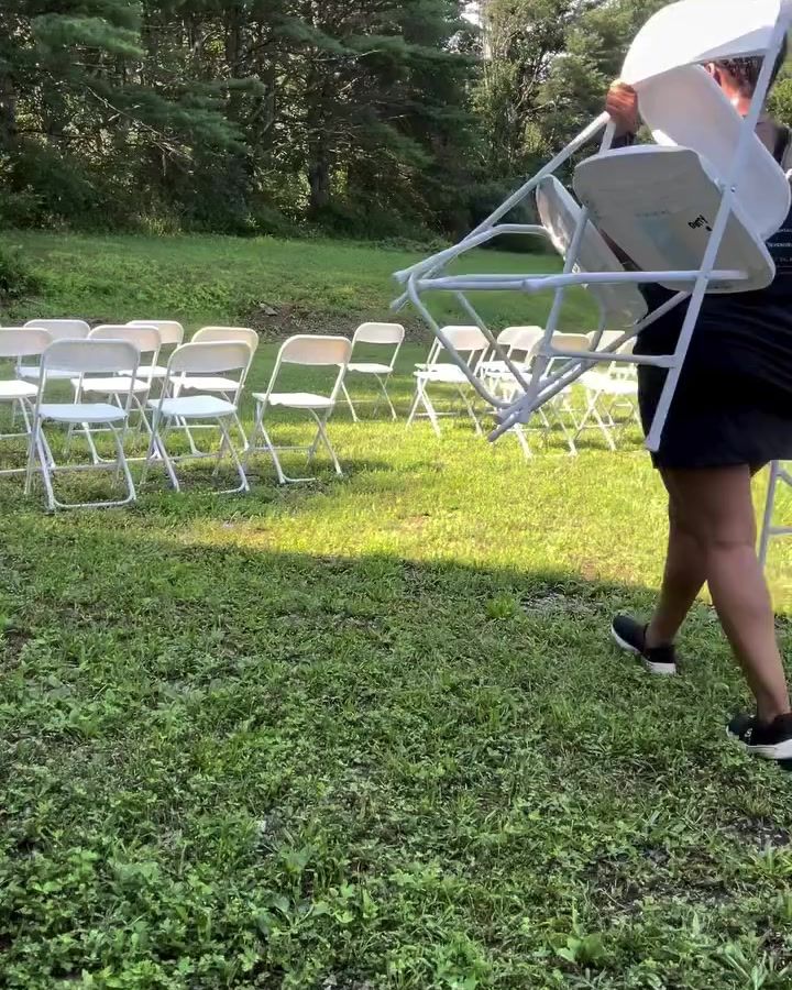 Patty carrying white folding chairs across a lawn to set up ceremony rows